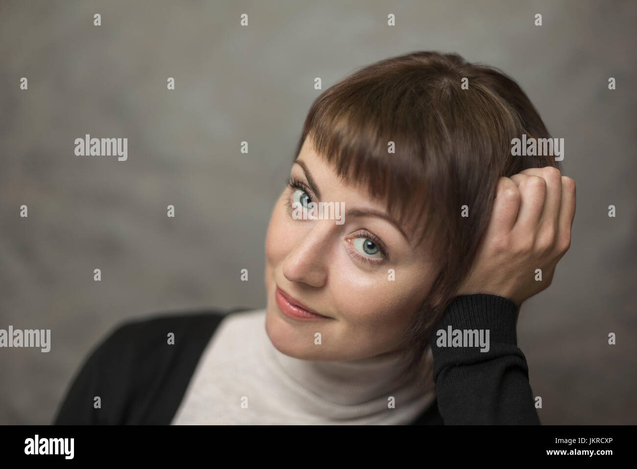 Portrait of smiling mid adult woman with head in hand against gray background Stock Photo