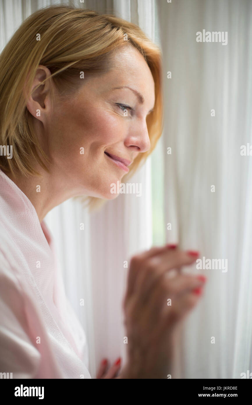 Smiling woman wearing bathrobe looking through window in bathroom Stock Photo