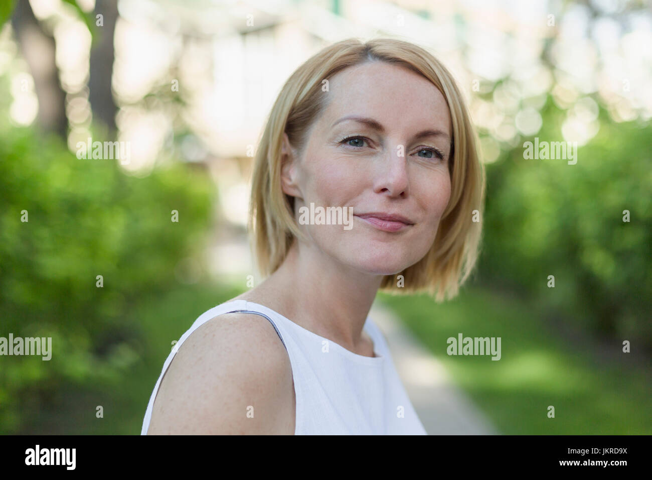 Close-up portrait of confident smiling mature woman with short blond hair at park Stock Photo