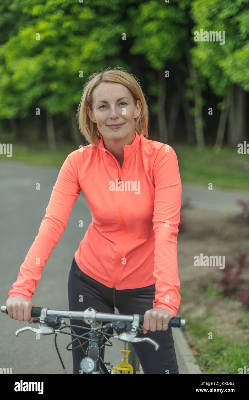 Portrait of smiling woman with bicycle on pathway at park against sky Stock Photo
