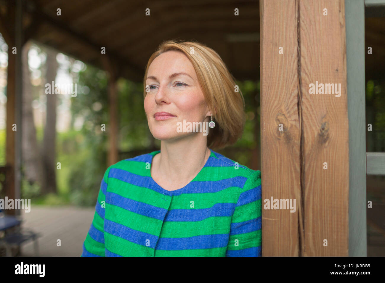 Thoughtful woman leaning on wooden wall in gazebo at park Stock Photo