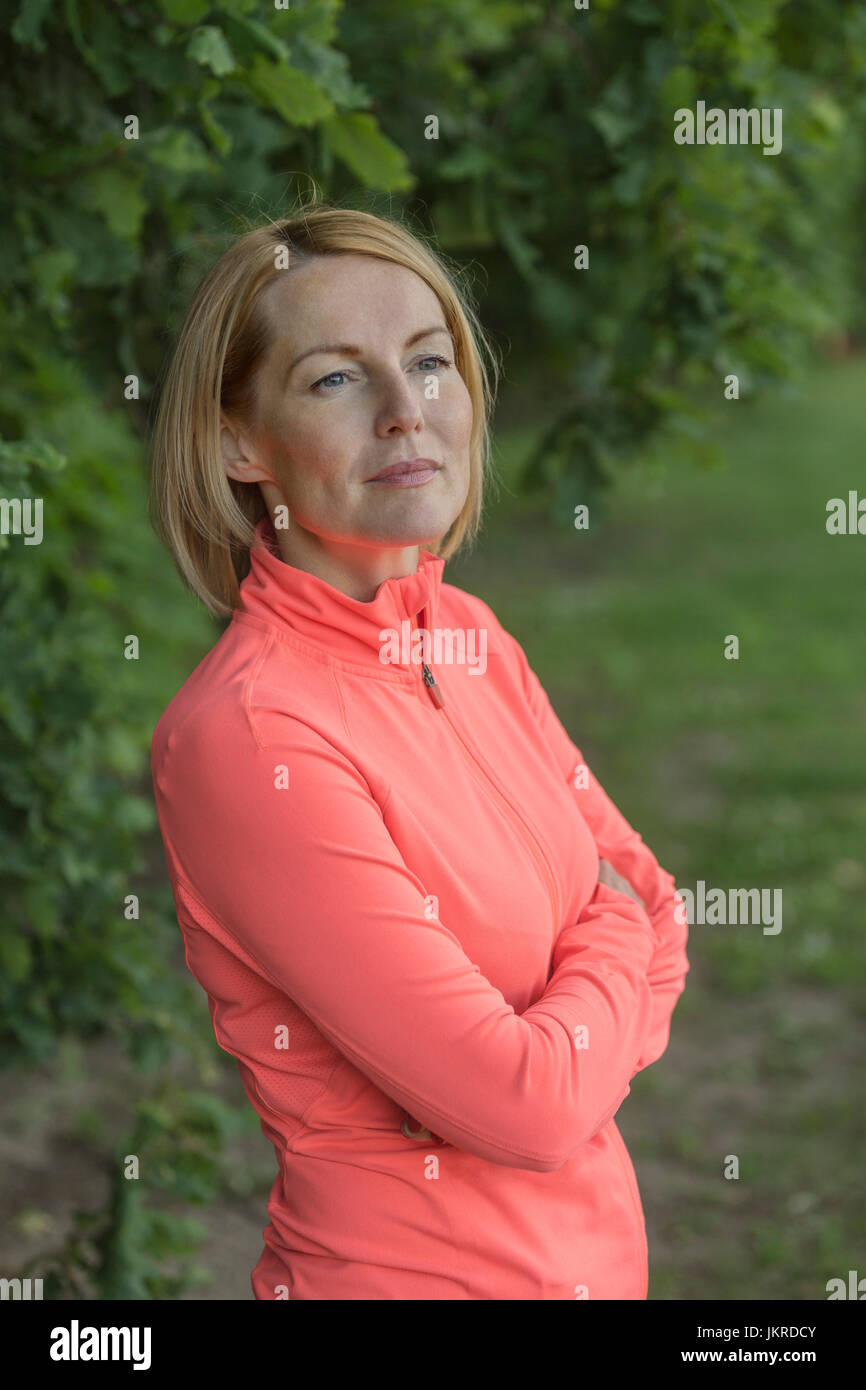 Thoughtful mature woman standing with arms crossed against trees at park Stock Photo