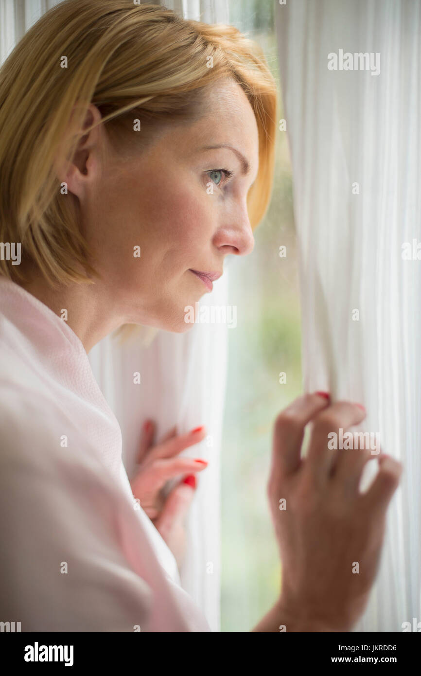Thoughtful woman wearing bathrobe looking through window in bathroom Stock Photo