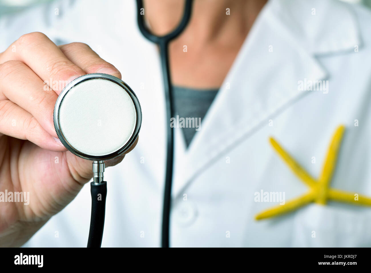 closeup of a young caucasian doctor man with a stethoscope in his hand and a colorful yellow starfish in the pocket of his white coat, depicting the m Stock Photo