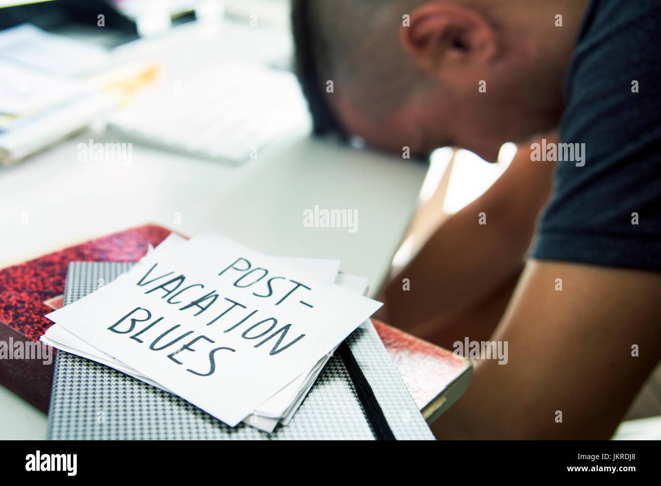 closeup of a concerned man sitting at his office desk and a note in the foreground with the text post-vacation blues handwritten in it Stock Photo