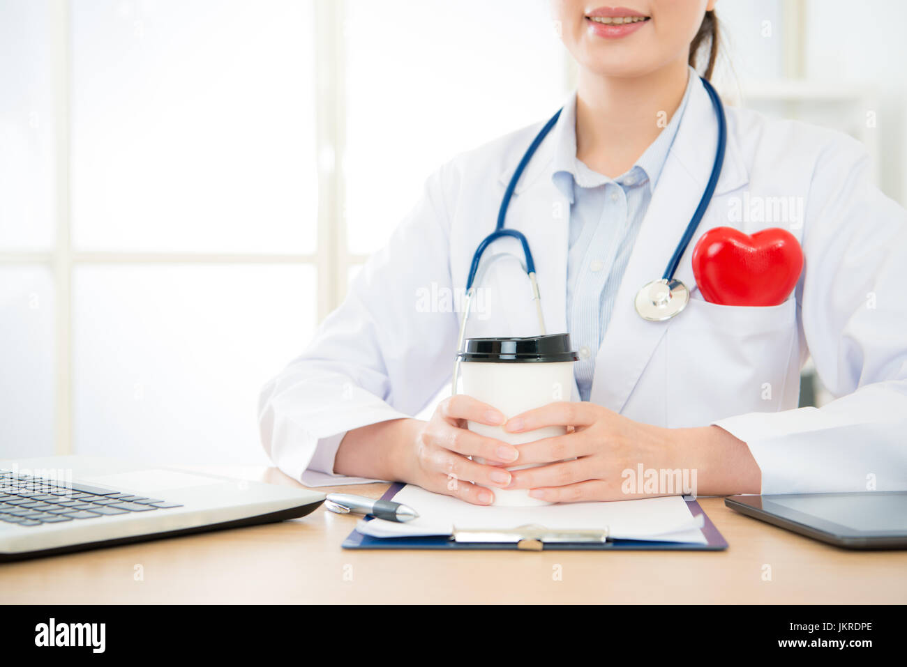 closeup photo of professional smiling doctor woman holding coffee cup working on cardiology office and offers online service for patient advisory palp Stock Photo