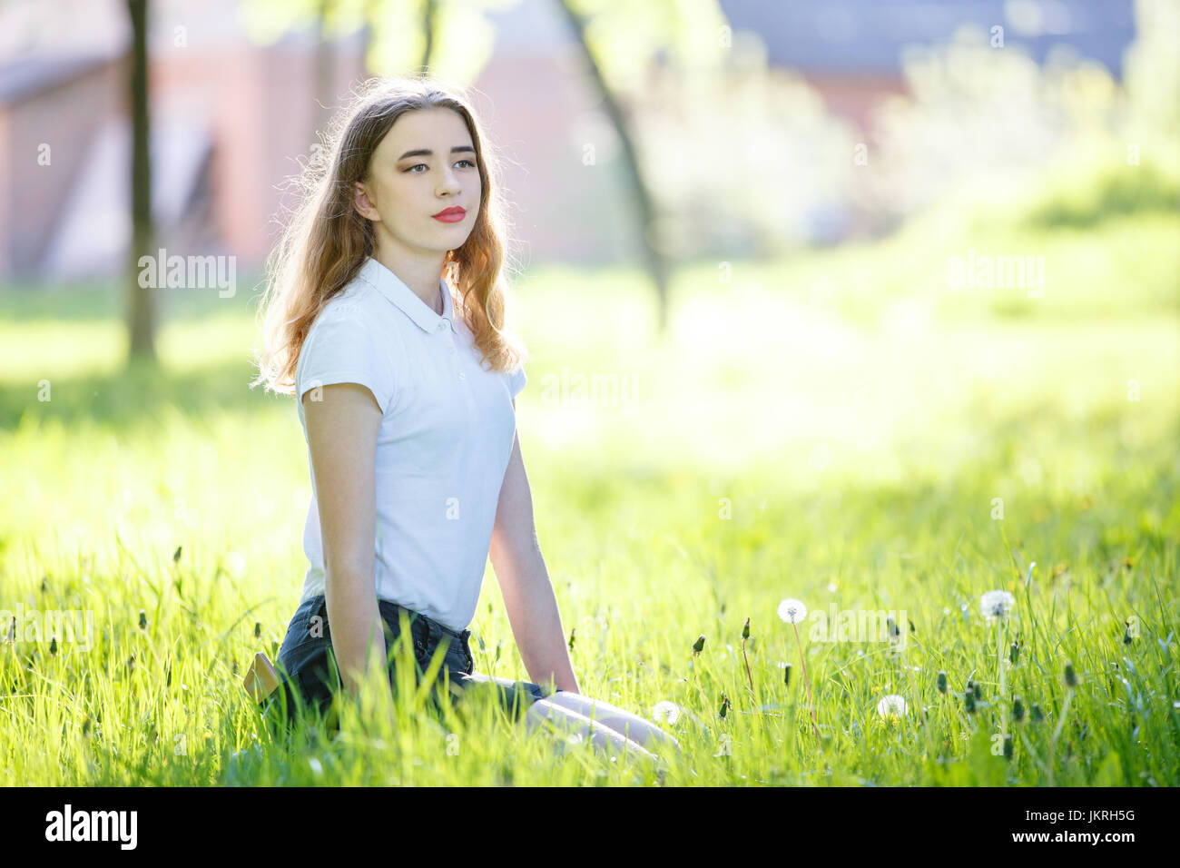 Young teenage girl sitting on green grass in sunny park. Image with copy space aside Stock Photo