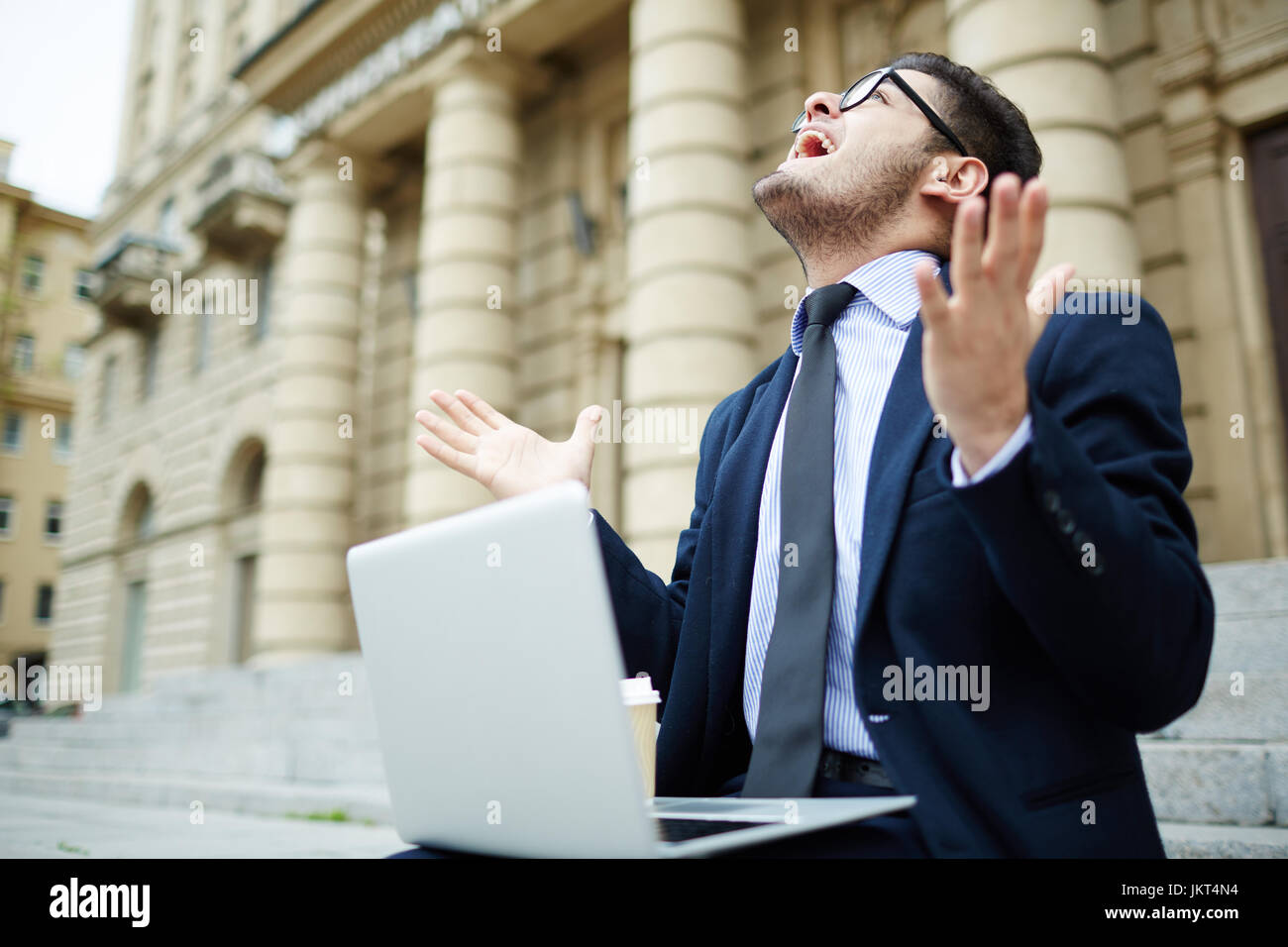 Excited businessman with laptop looking upwards and expressing gladness Stock Photo