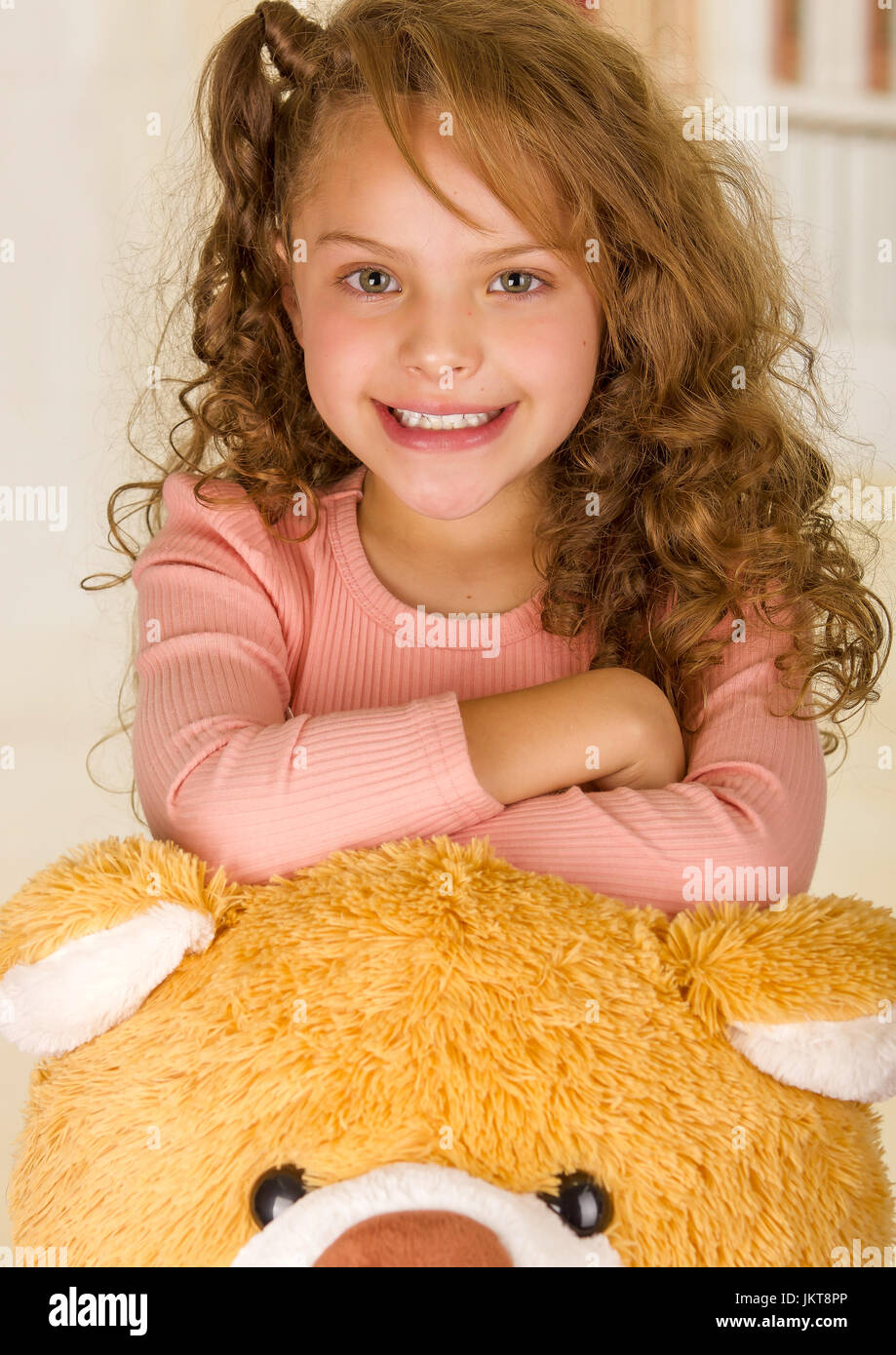 A portrait of a young pretty girl smiling and posing over her teddy bear head in a doctor office background Stock Photo