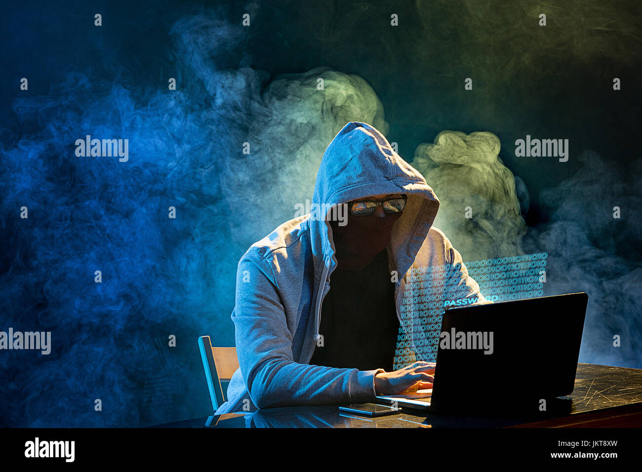 Hooded computer hacker stealing information with laptop Stock Photo