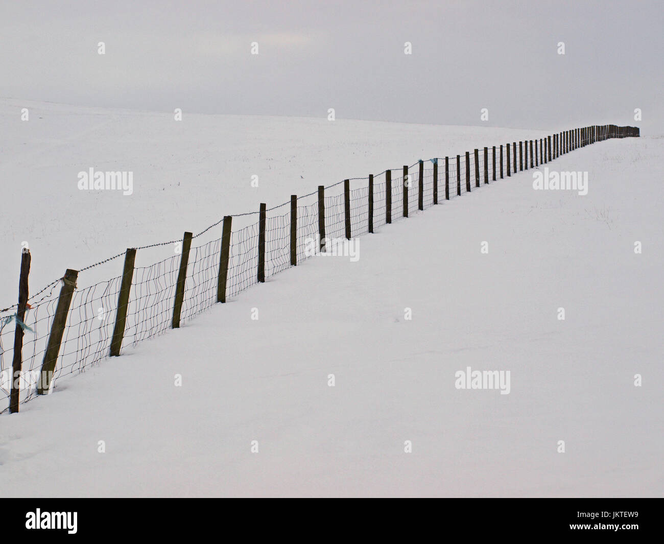 wire and post fence receding starkly to the skyline in snowy landscape in Cumbria, England, UK Stock Photo