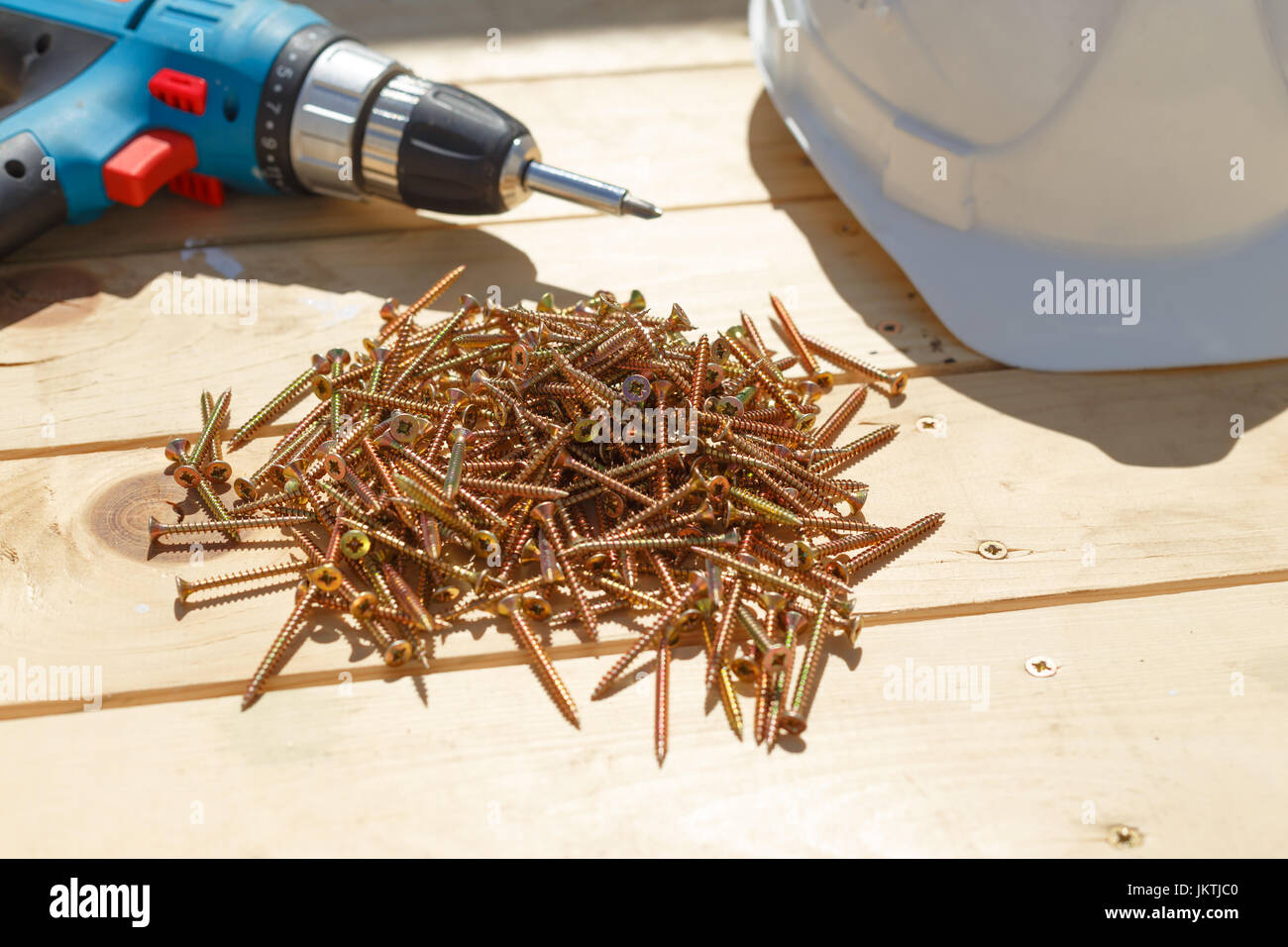 Tools for the construction of a wooden floor or terrace. Screwdriver, self-tapping screws and helmet on the wooden floor. View from above. Stock Photo