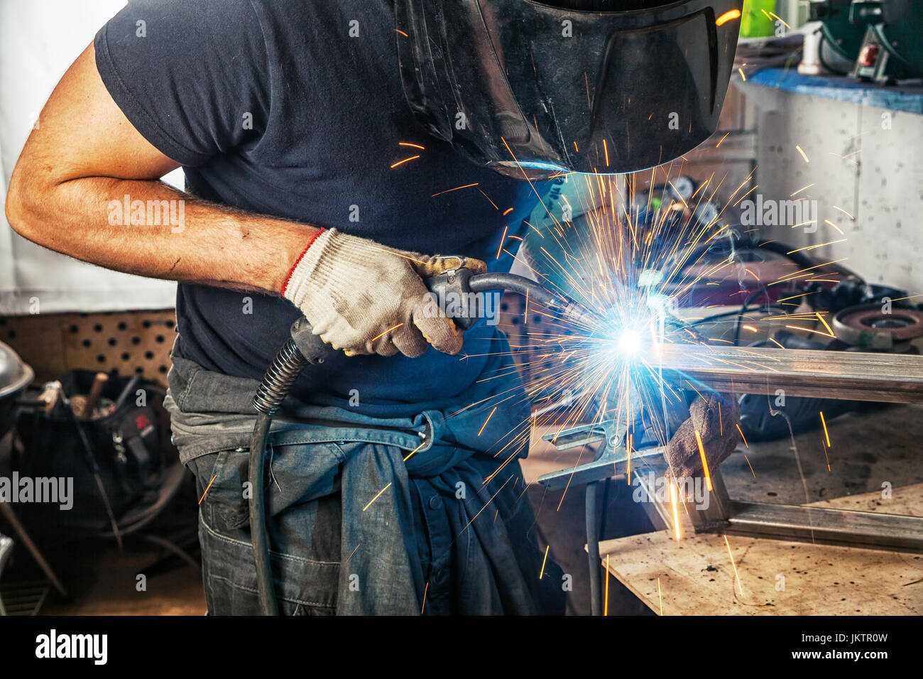 A man welder in a black Tshirt, construction gloves and a welding mask