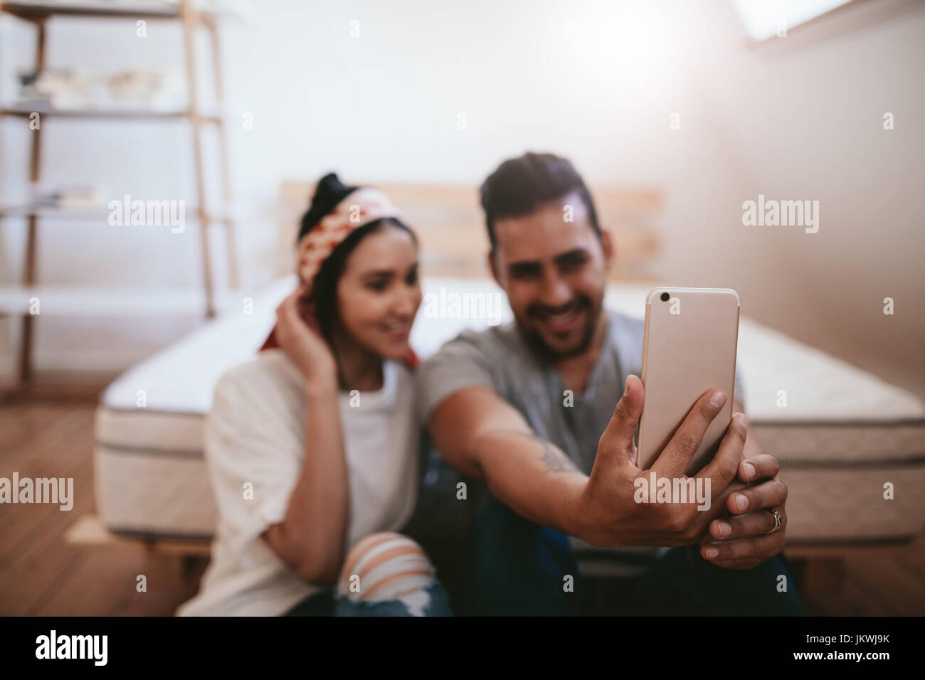 Shot of young couple sitting at home and taking selfie with mobile phone. Focus on smart phone in hands of a man. Stock Photo