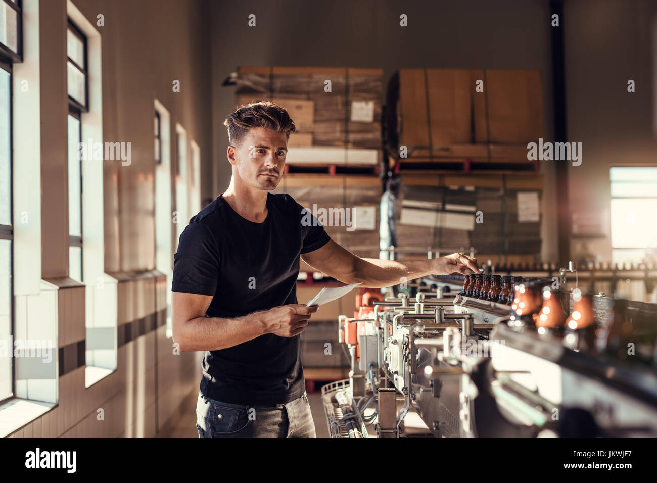 Brewer examining the beer production in brewery plant. Young man standing at the beer bottling machine in factory. Stock Photo