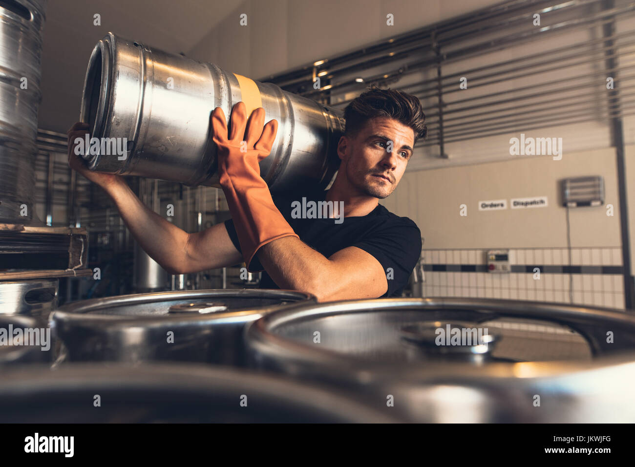 Shot of brewer carrying keg at brewery factory. Young man with metal beer barrels at warehouse. Stock Photo