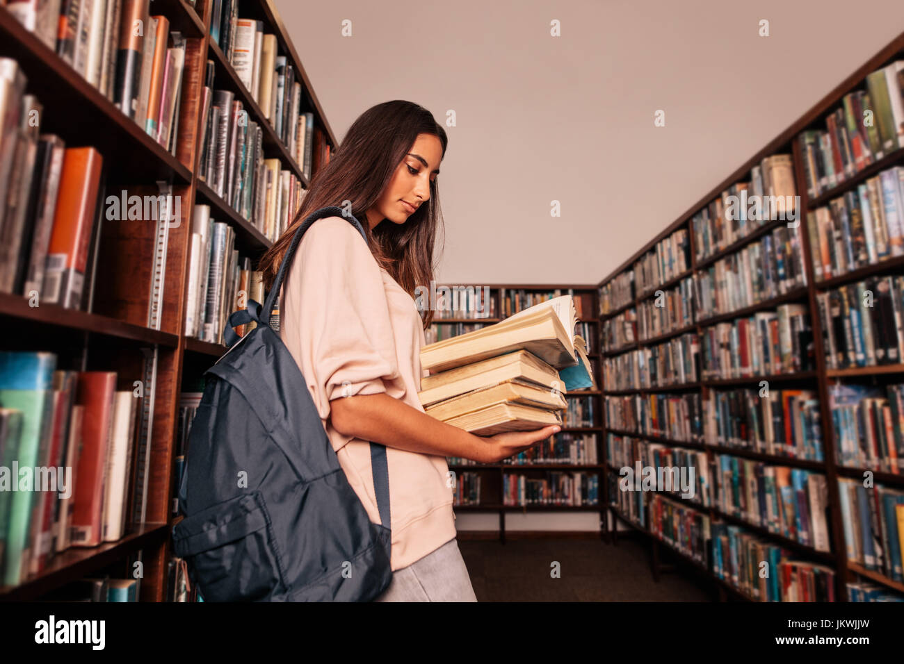 Young female student carrying lots of books in the college library