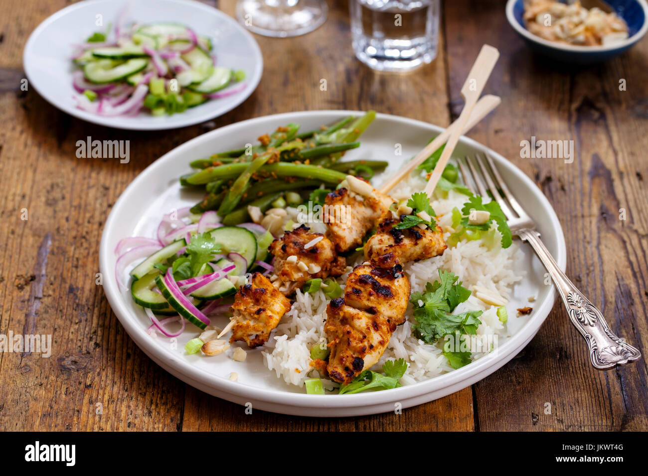 Satay chicken skewers with rice, cucumber salad and green beans Stock