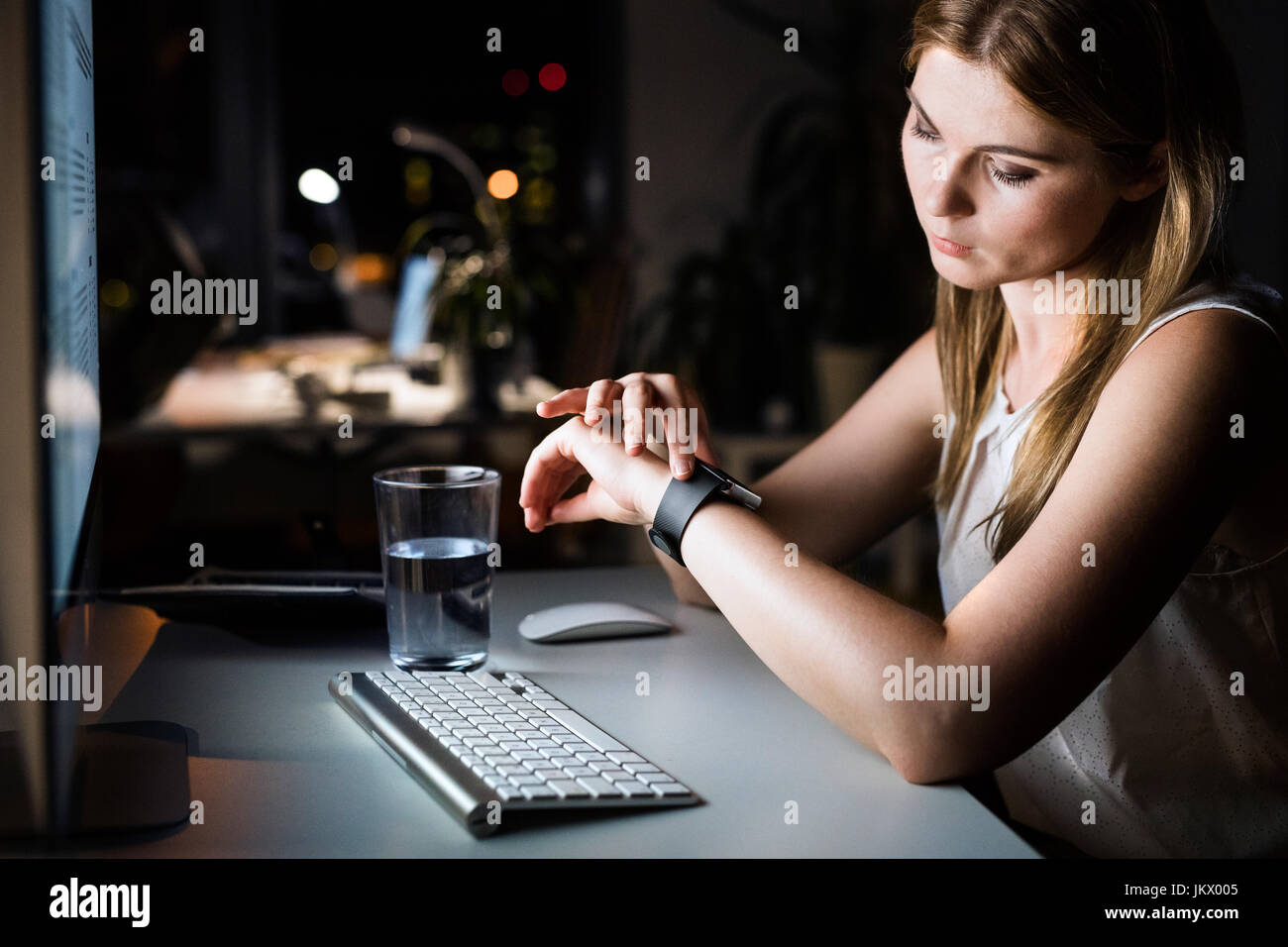 Businesswoman in her office at night looking at watch. Stock Photo