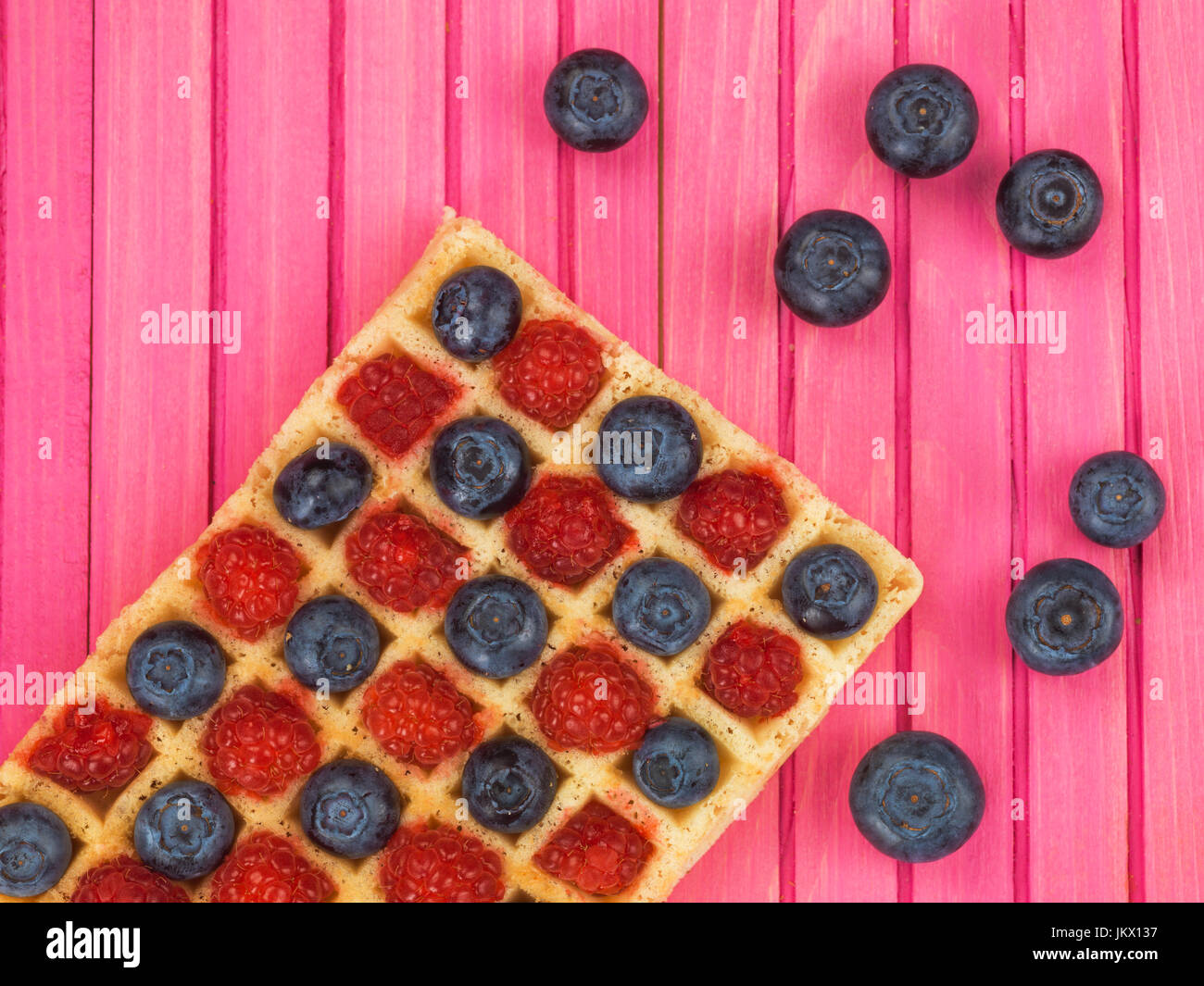 Raspberries and Blueberries on a Toasted Waffle Against a Pink Wooden Background Stock Photo