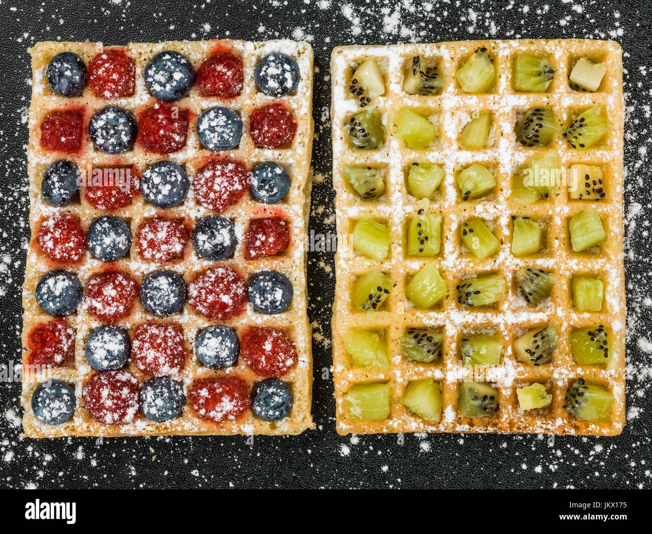 Fruit Waffles with Raspberries Blueberries and Kiwi Fruit and Icing Sugar Against a Black Background Stock Photo
