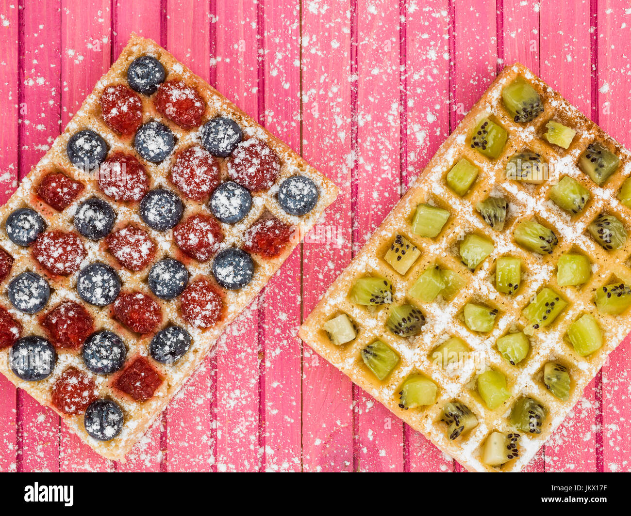 Fruit Waffles with Raspberries Blueberries and Kiwi Fruit and Icing Sugar Against a Pink Wooden Background Stock Photo
