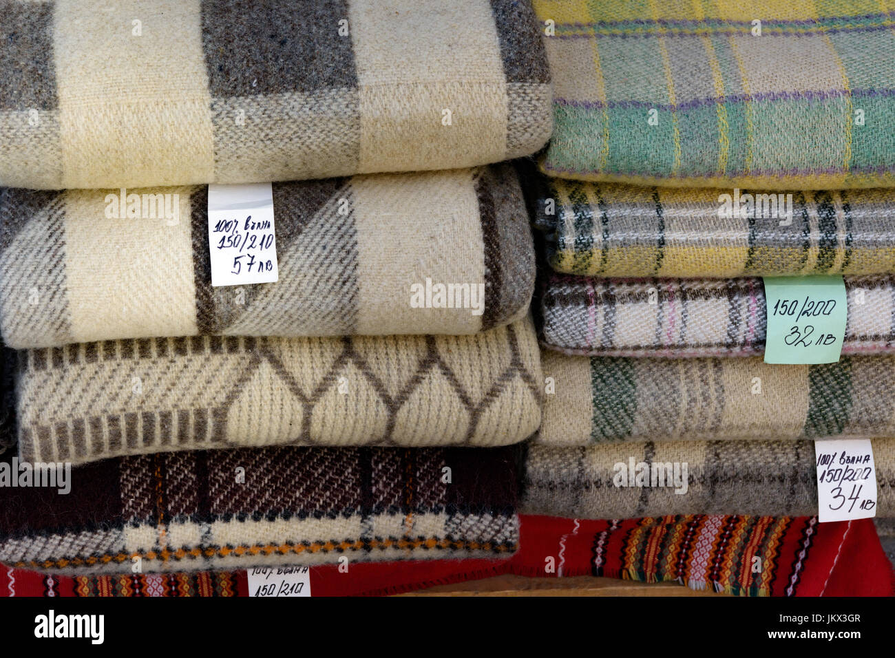 Stacked folded blankets for sale with price tags in bulgarian language. The foreign text translates as 100% wool Stock Photo