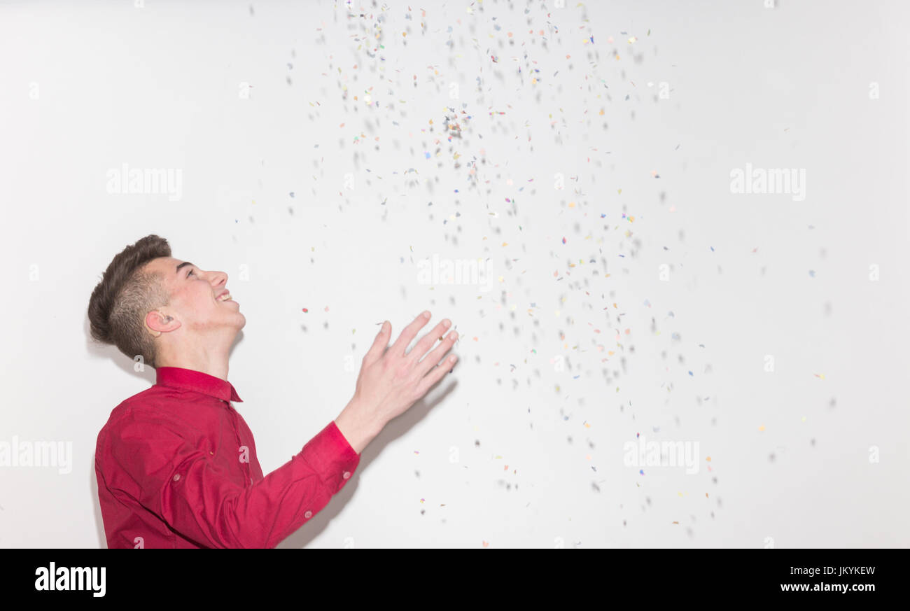 side view, profile portrait, one teenager boy, looking up, looking above, throwing confetti falling, white background studio, red shirt, upper body sh Stock Photo