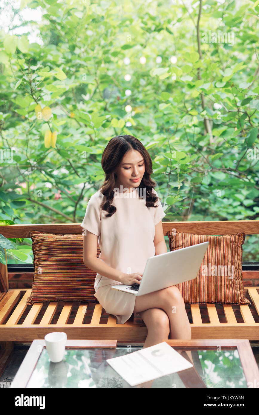 Beautiful young smiling woman working on laptop while sitting on bed at ...