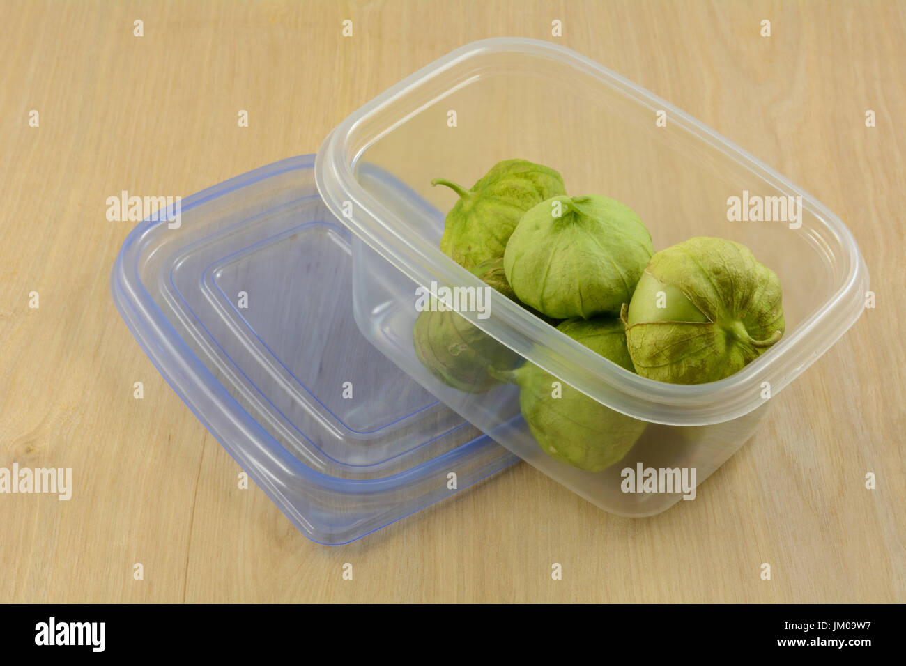 Green tomatillos in husks in plastic refrigerator storage container on