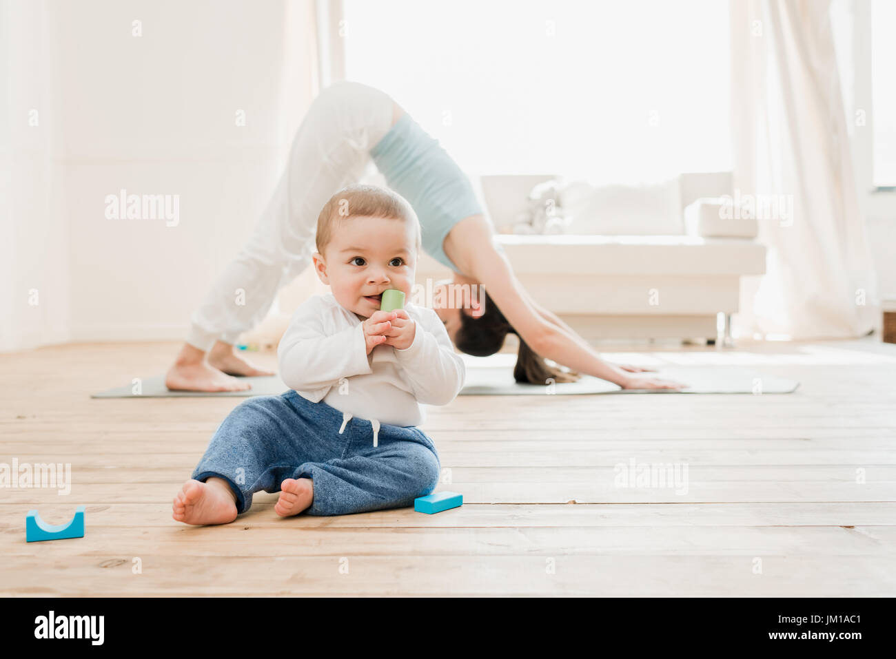 Young woman in downward dog position while her baby playing at home