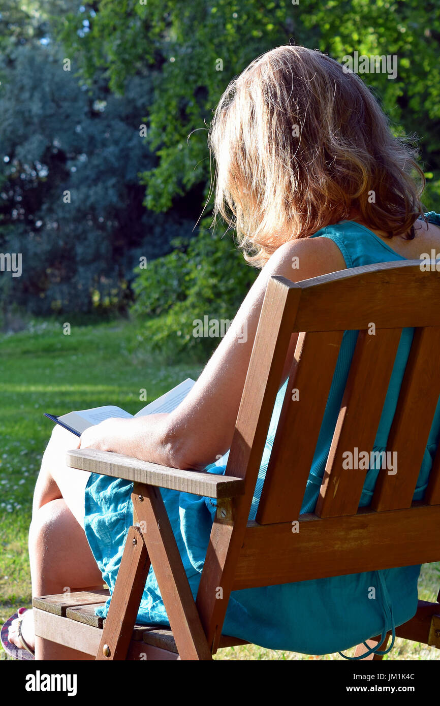 Woman reading book in a garden and enjoying the last rays of evening sunlight on summer. Stock Photo
