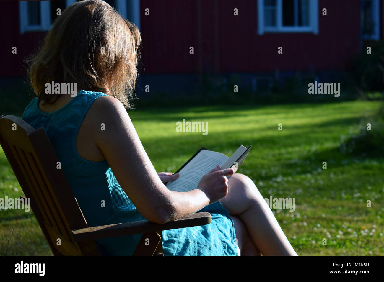 Woman reading book in a garden and enjoying the last rays of evening sunlight on summer. Stock Photo