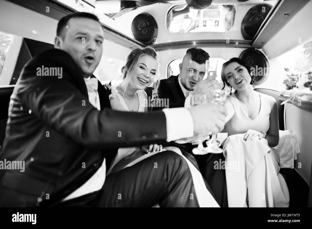 Groomsmen and bridesmaids drinking champagne in the limo. Black and white photo. Stock Photo