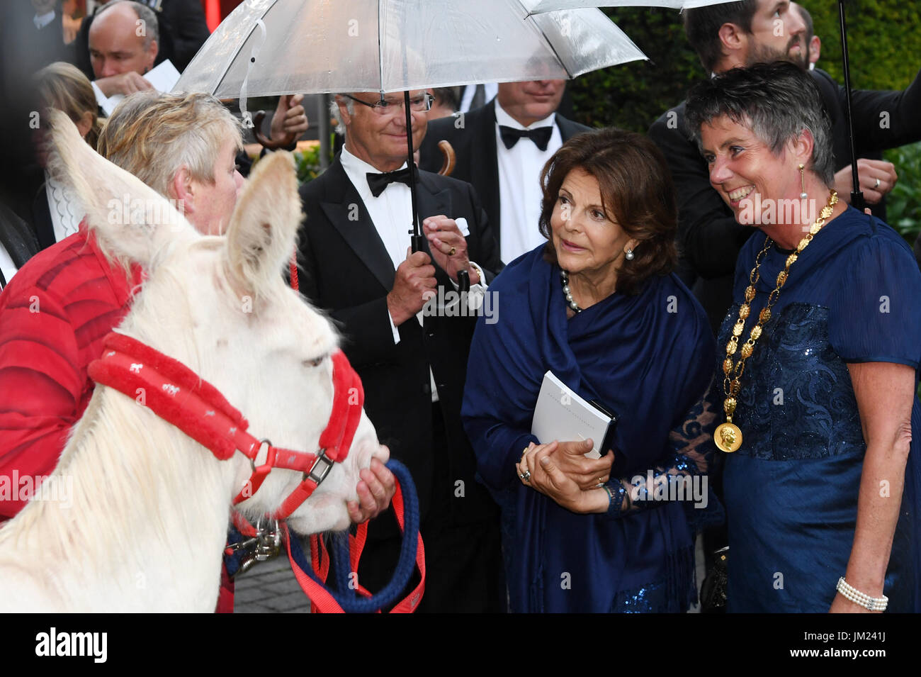 Bayreuth, Germany. 25th July, 2017. Mayoress of Bayreuth Brigitte Merk-Erbe (r-l), Sweden's Queen Silvia, Sweden's King Carl Gustaf (with umbrella) and a staff member from the Neusiedler See National Park with a white donkey, pictured at the opening of the Bayreuth Festival in Bayreuth, Germany, 25 July 2017. The donkey was brought into the garden of the Festspielhaus by the national park staff to show the Swedish royal couple. Photo: Tobias Hase/dpa/Alamy Live News Stock Photo