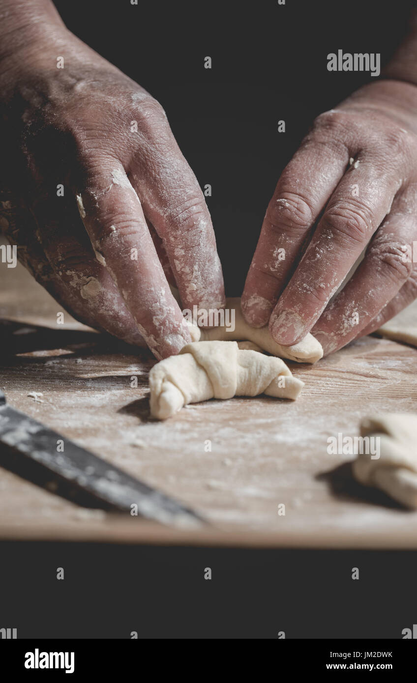 Senior woman, grandma, rolling fresh homemade croissants. Vertical orientation. Close up on working old hands. Saturated, subdued colors Stock Photo