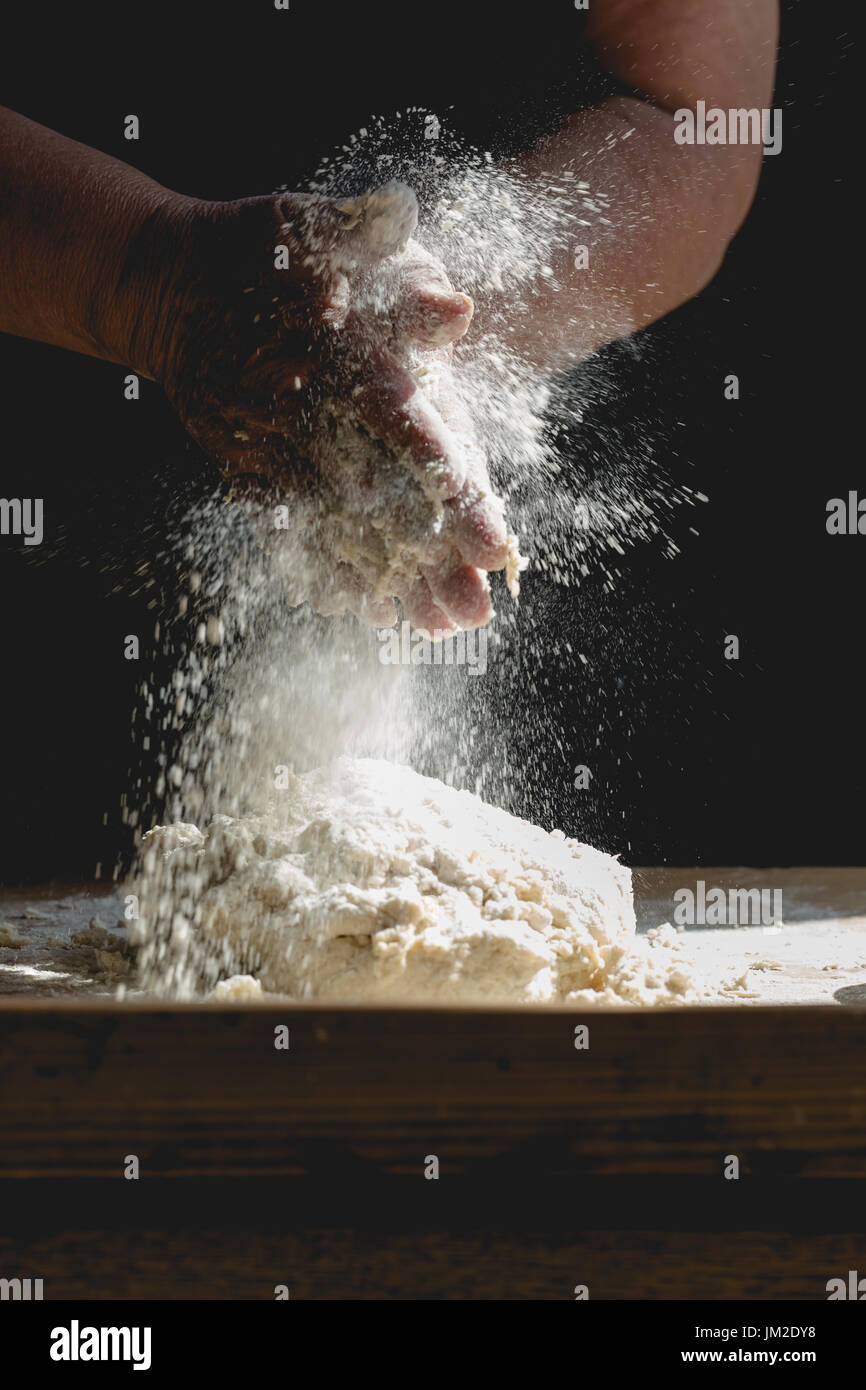 Grand mother kneading pastry for Christmas baking, making splash from flour. Vertical crop, faded colours with selective focus on working old hands an Stock Photo