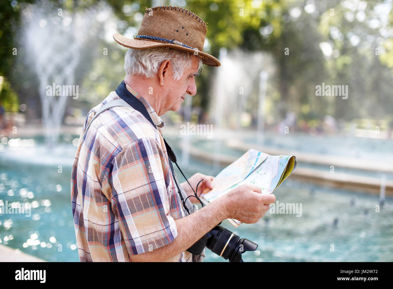 Pensioner tourist in hat searching for destination on map in park with fountains Stock Photo