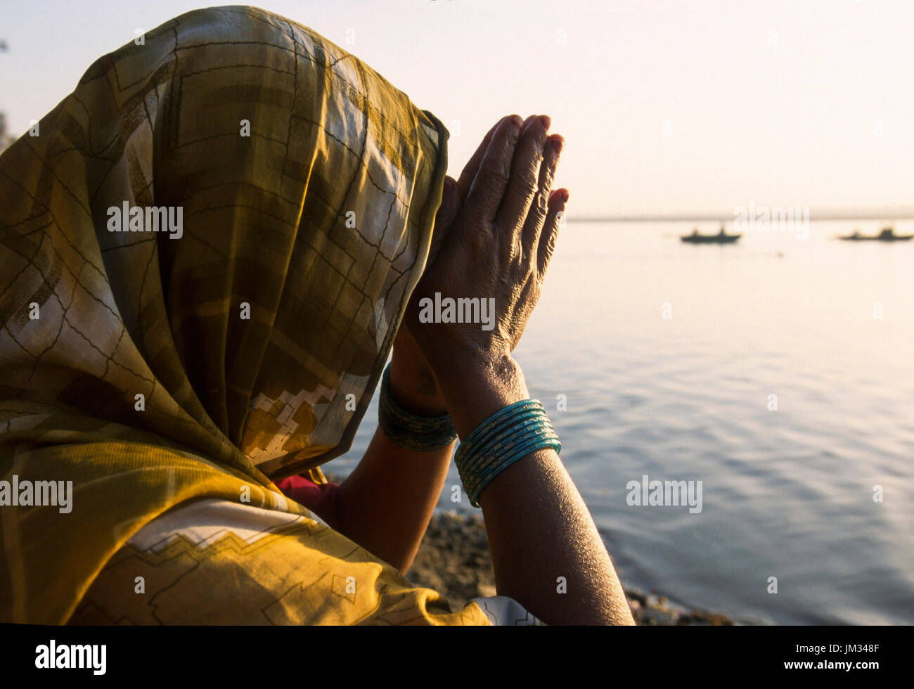 INDIA, Uttar Pradesh, Varanasi, Hindu woman folding hand for morning prayer for Lord shiva and goddess ganga at river Ganges, facing the sunrise, the old Banaras or Kashi or ANANDAVANA ( forest of bliss ) is a sacred place for Hindus to achieve Moksha meaning salvation from eternal circle of rebirth, the Ganga river is a crossing place from earth to heaven, a very religious place for enlightenment bliss devotion purification Stock Photo