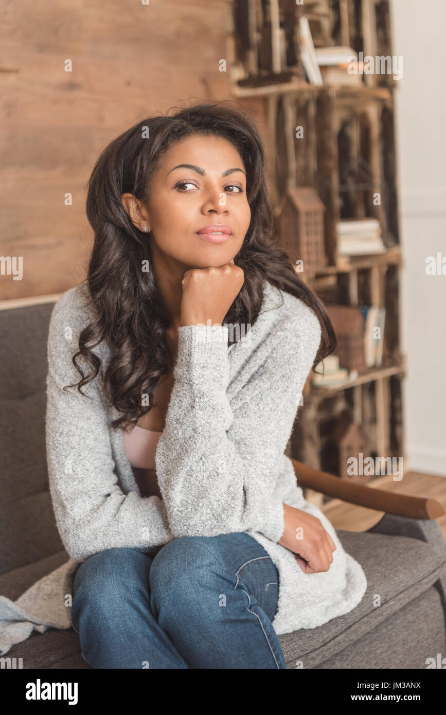 Portrait of beautiful young african american woman sitting on couch and ...