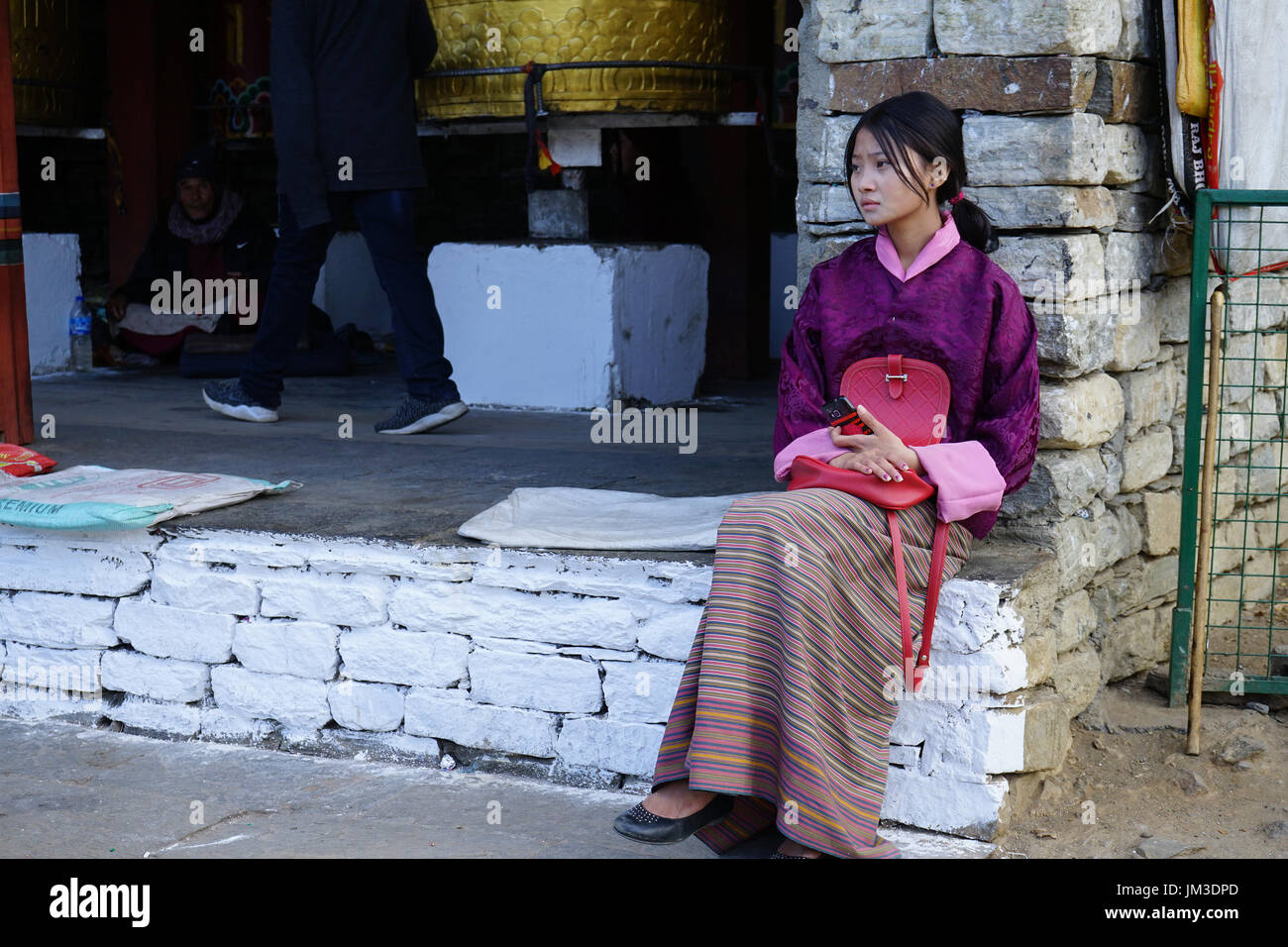 Girl with sad expression sitting with cellphone and traditional dress at the Timphu Memorial Chörten, Bhutan Stock Photo