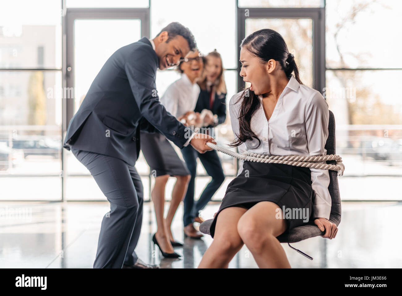 asian businesswoman bound with rope on chair and multicultural business team pulling her, team spirit business concept Stock Photo