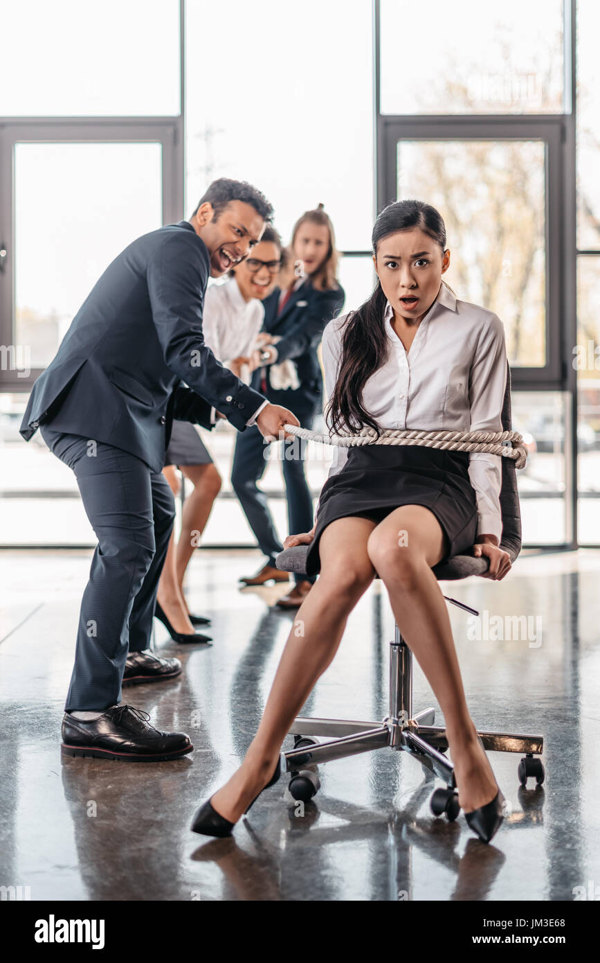 asian businesswoman bound with rope on chair and multicultural business team pulling her, team spirit business concept Stock Photo