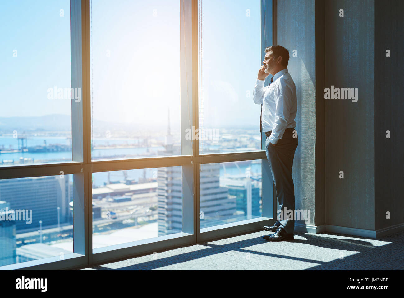 Mature and cnofident business executive looking looking out of large windows at a view of the city below, from the top floor of an office building, wh Stock Photo