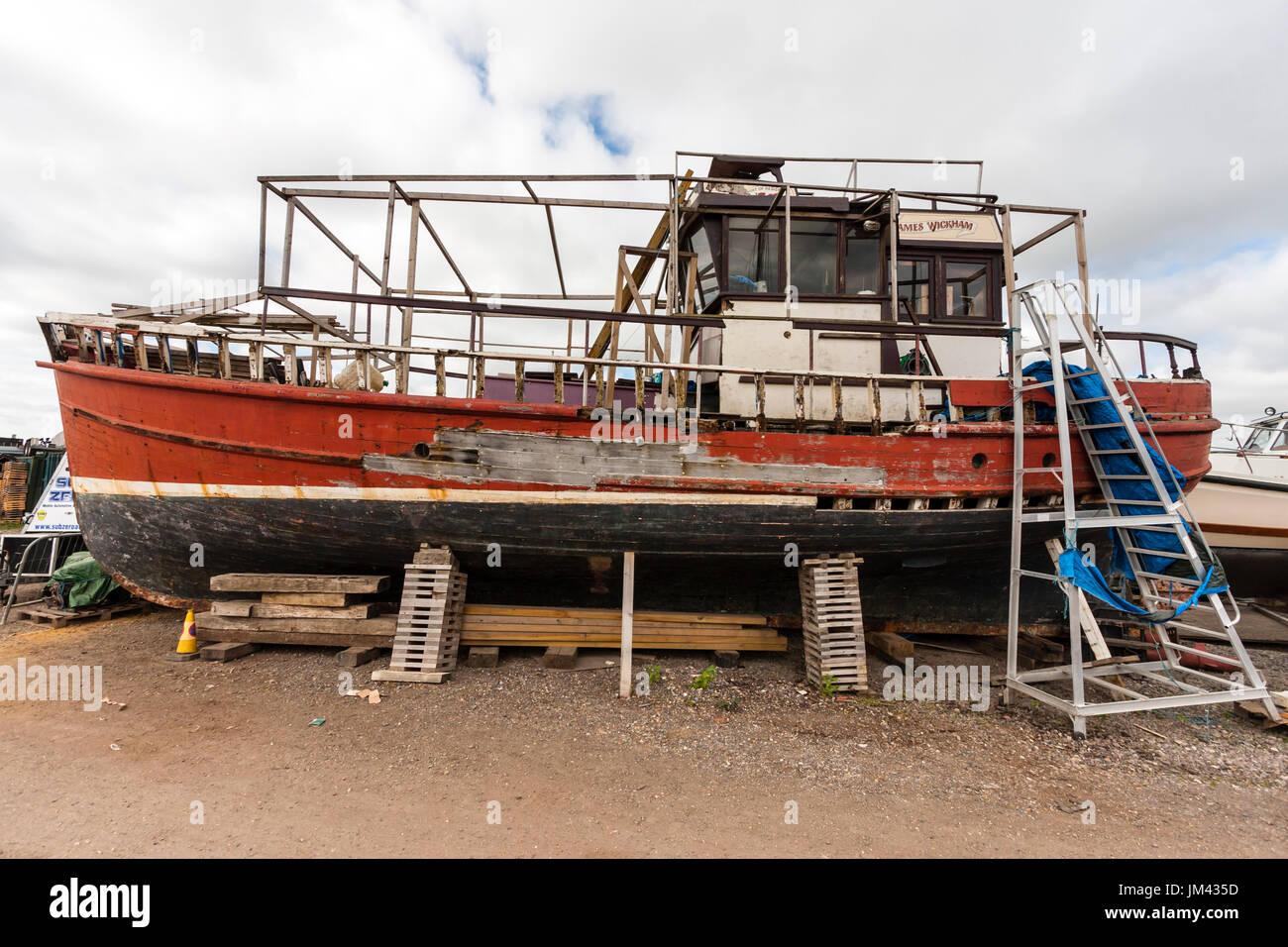 Former fishing boat, red hull, supported by timbers on land and in state of  did-repair and weathering. Parts of hull holed, paint stripped in places  Stock Photo - Alamy