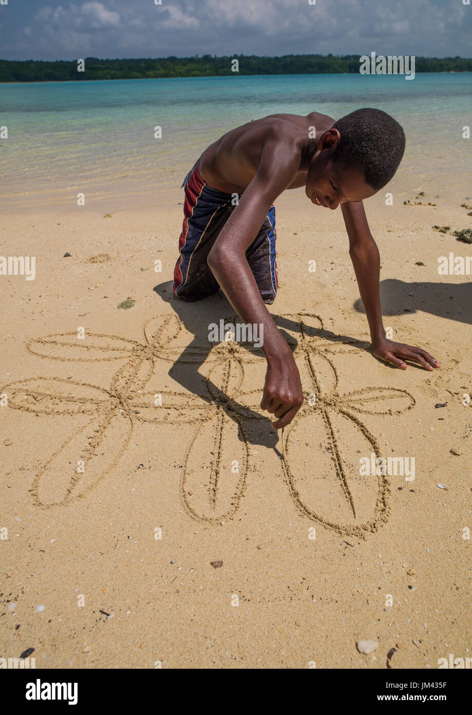 Boy on the beach making a traditional sand drawing, Sanma Province