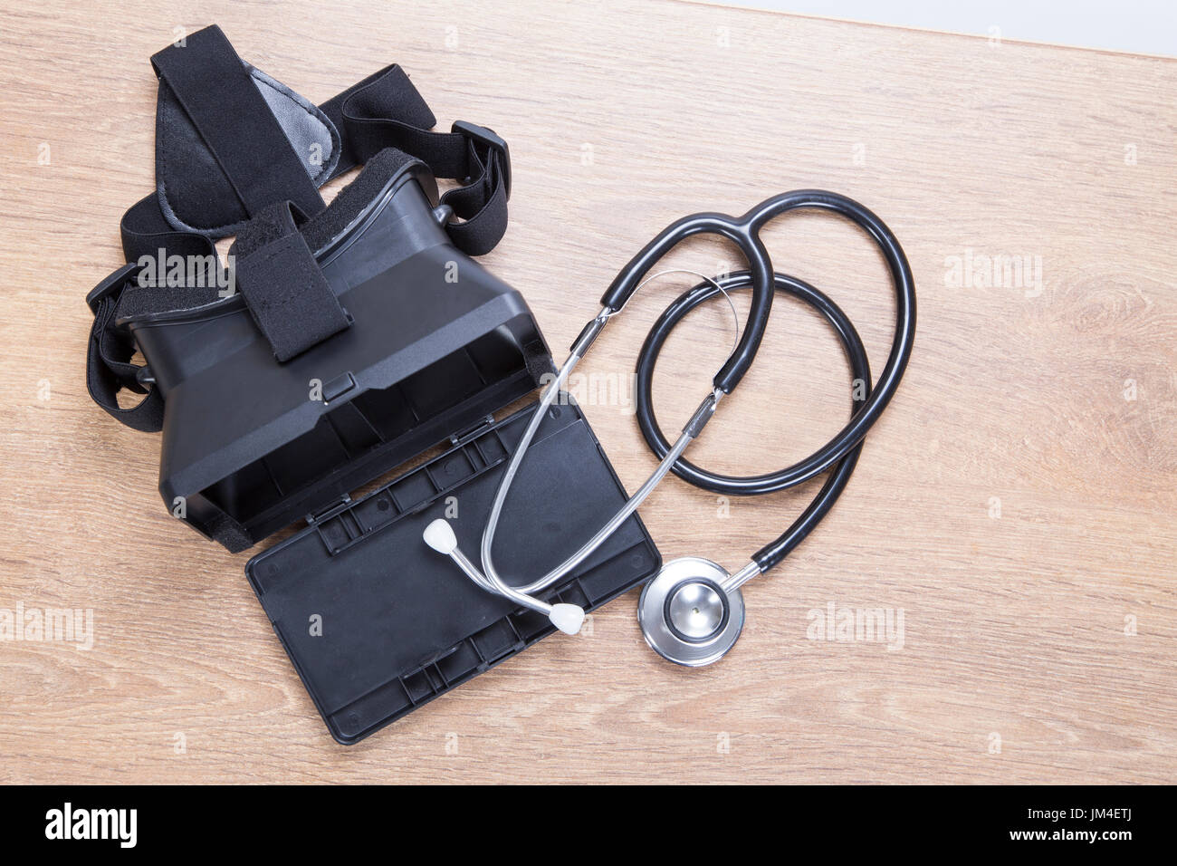 3d VR virtual reality headset with a coiled stethoscope lying together on a wooden table in a diagnostics, repair and maintenance concept Stock Photo