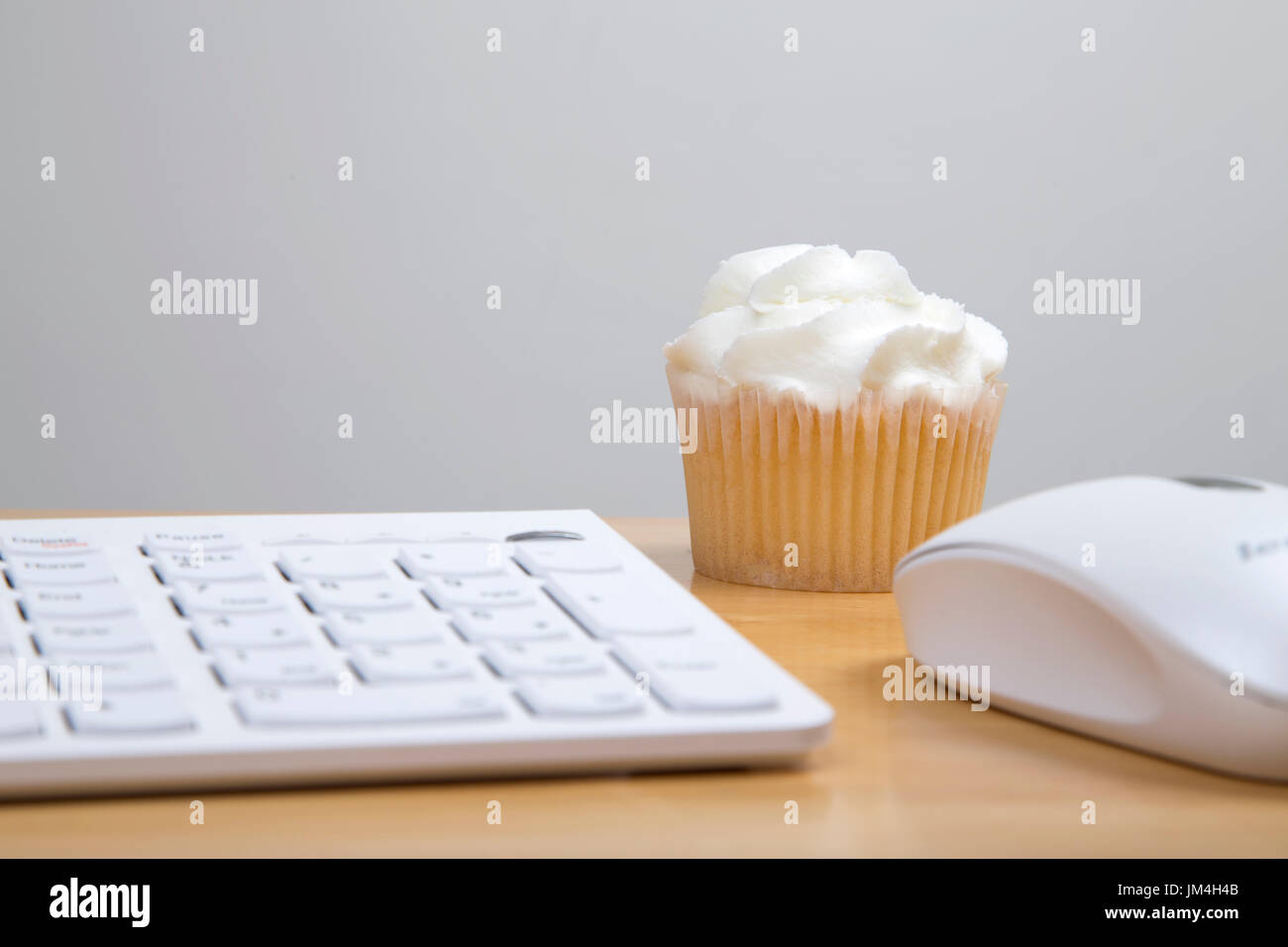 Butter icing cupcake sitting on work desk with keyboard and mouse Stock Photo