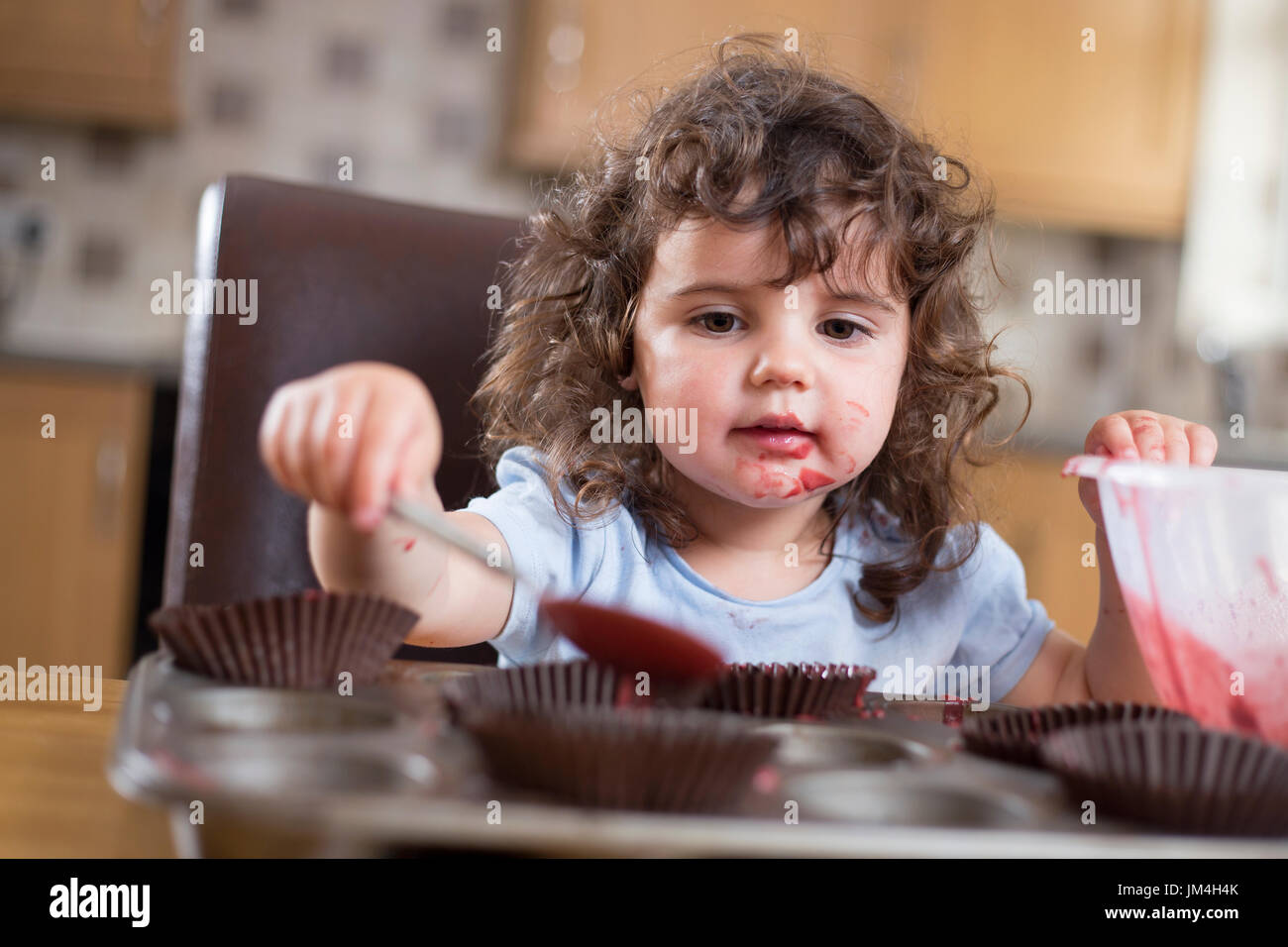 Two year old girl placing cake batter into cake paper Stock Photo Alamy