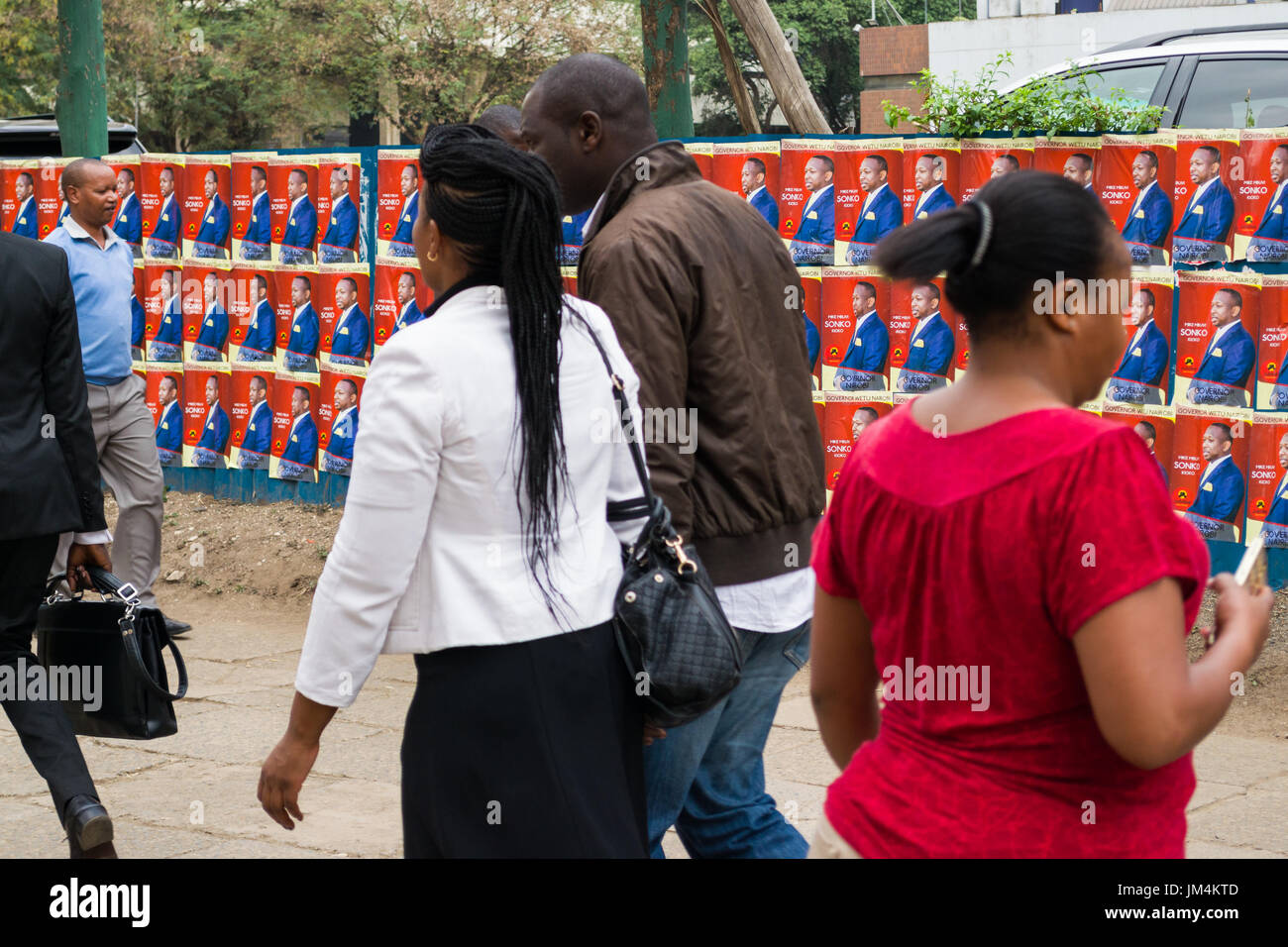 People Walking Past Kenyan Election Candidate Posters On Wall In Nairobi City, Kenya Stock Photo